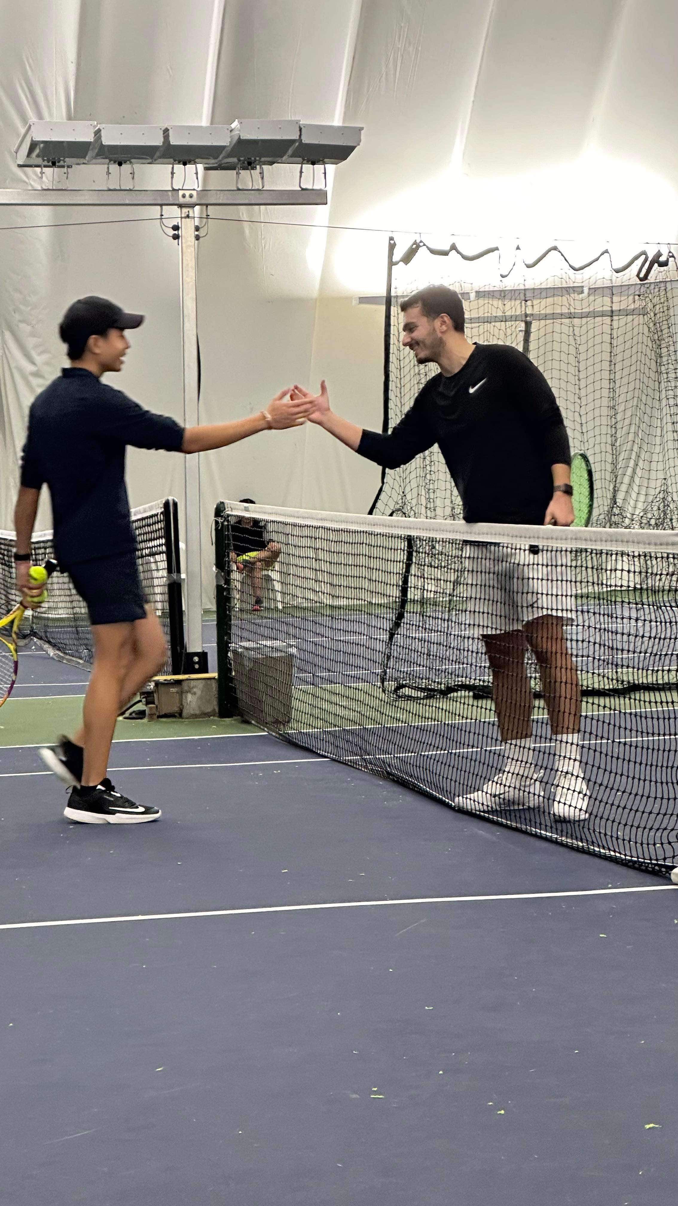 Two tennis club members shaking hands over the net.